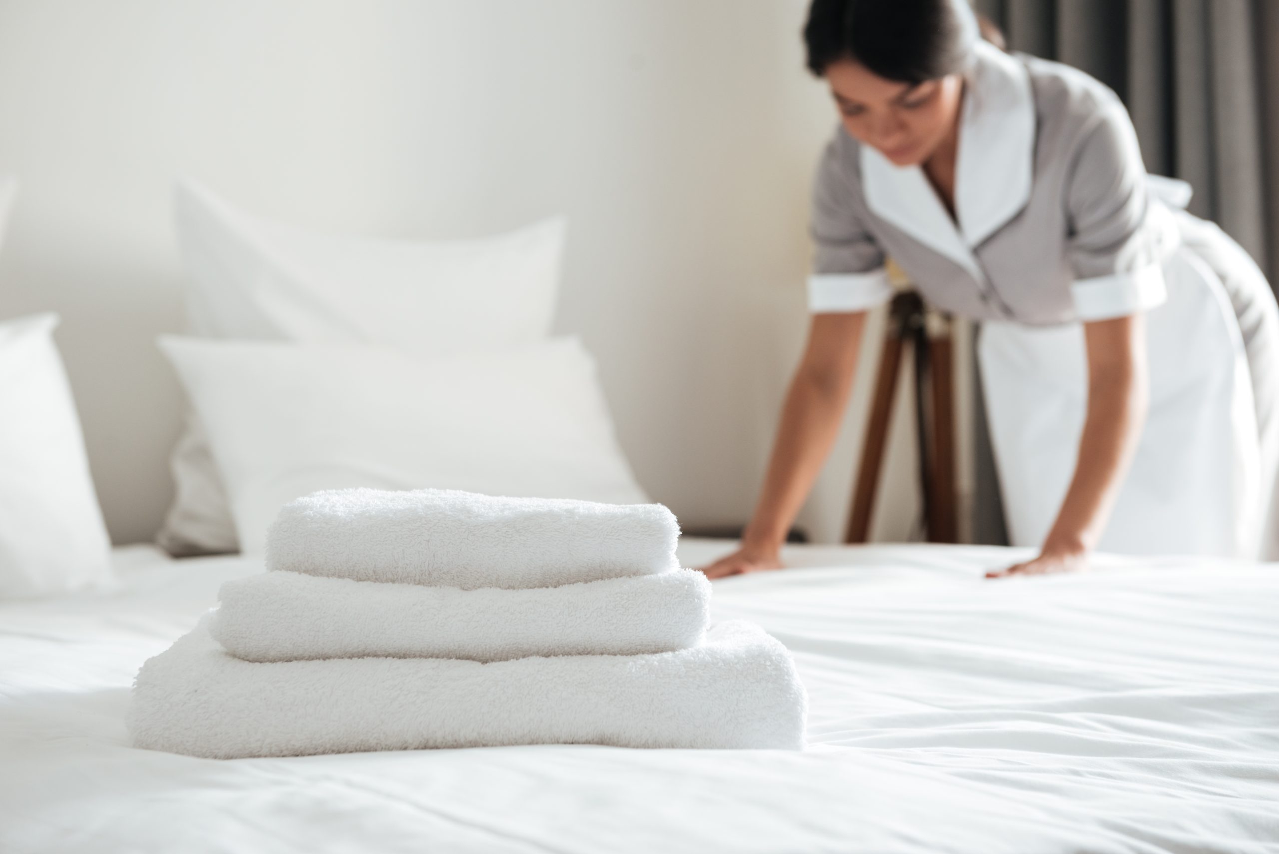 young hotel maid setting up pillow on bed scaled