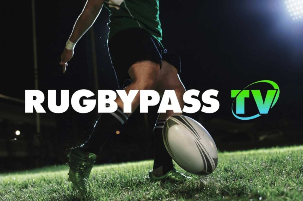 Jogador de rugby em campo segurando a bola durante partida noturna, com destaque para a marca RugbyPass TV como plataforma para assistir jogos ao vivo online.