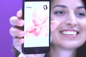 Aplicativo Pregnancy+: O Companheiro Definitivo das Futuras Mamães 14 Mulher sorrindo enquanto mostra o Aplicativo Pregnancy no celular, exibindo imagem do bebê e informações sobre a gestação em tempo real.