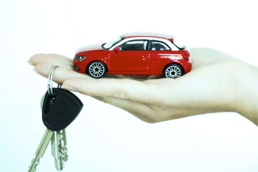 Chave de carro e miniatura de veículo vermelho sobre uma mão estendida, representando segurança, compra e verificação de informações do veículo.