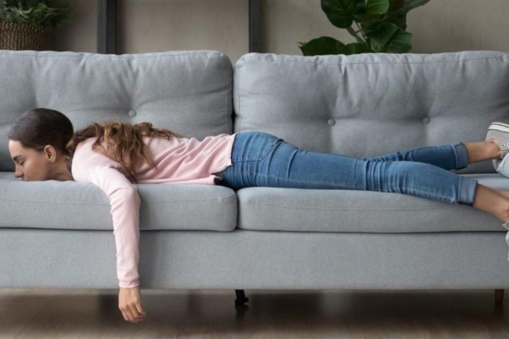 Primeiros Sinais de Gravidez: Como Identificar os Sintomas Iniciais e Confirmar com Segurança 4 Mulher deitada exausta no sofá, representando o cansaço e a fadiga intensa como um dos primeiros sinais de gravidez nas primeiras semanas