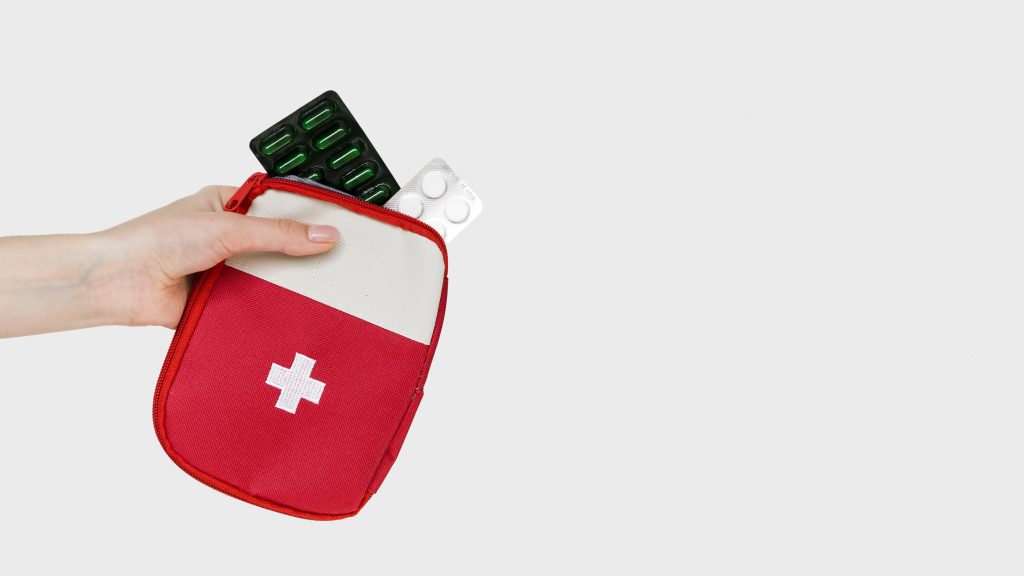 Mala de viagem aberta com um kit de medicamentos organizado, incluindo itens básicos de primeiros socorros e produtos de higiene, representando como escolher e levar seus medicamentos de viagem de forma segura e prática.