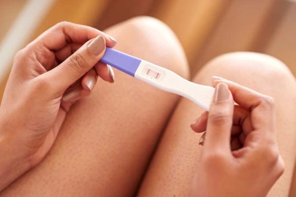 Mulher segurando teste de gravidez positivo, representando um dos primeiros sinais de gravidez e a confirmação das suspeitas nas primeiras semanas de gestação