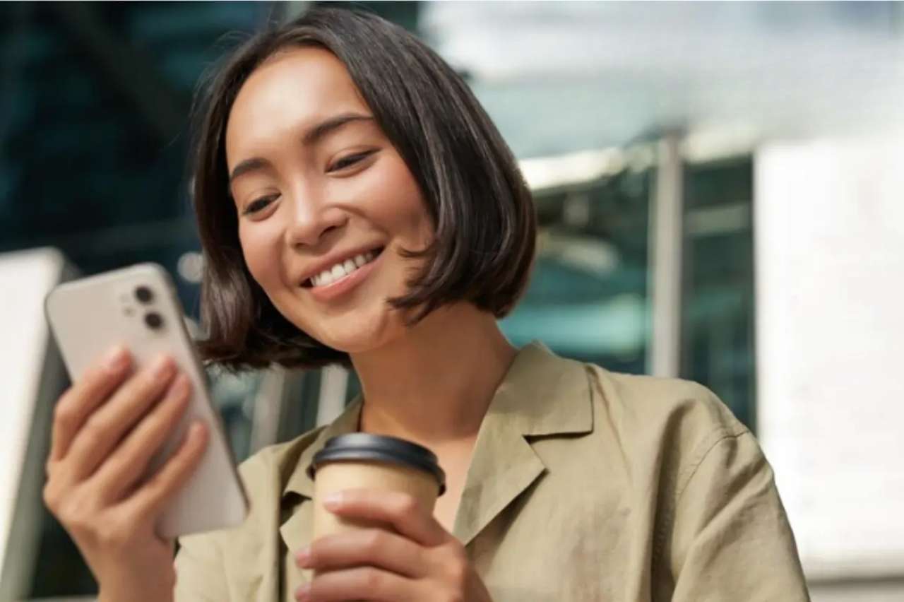 Os melhores aplicativos gratuitos para assistir futebol internacional no celular em 2026 6 Mulher sorrindo enquanto usa o smartphone, representando a praticidade de assistir futebol pelo celular em qualquer lugar de forma simples e conveniente.